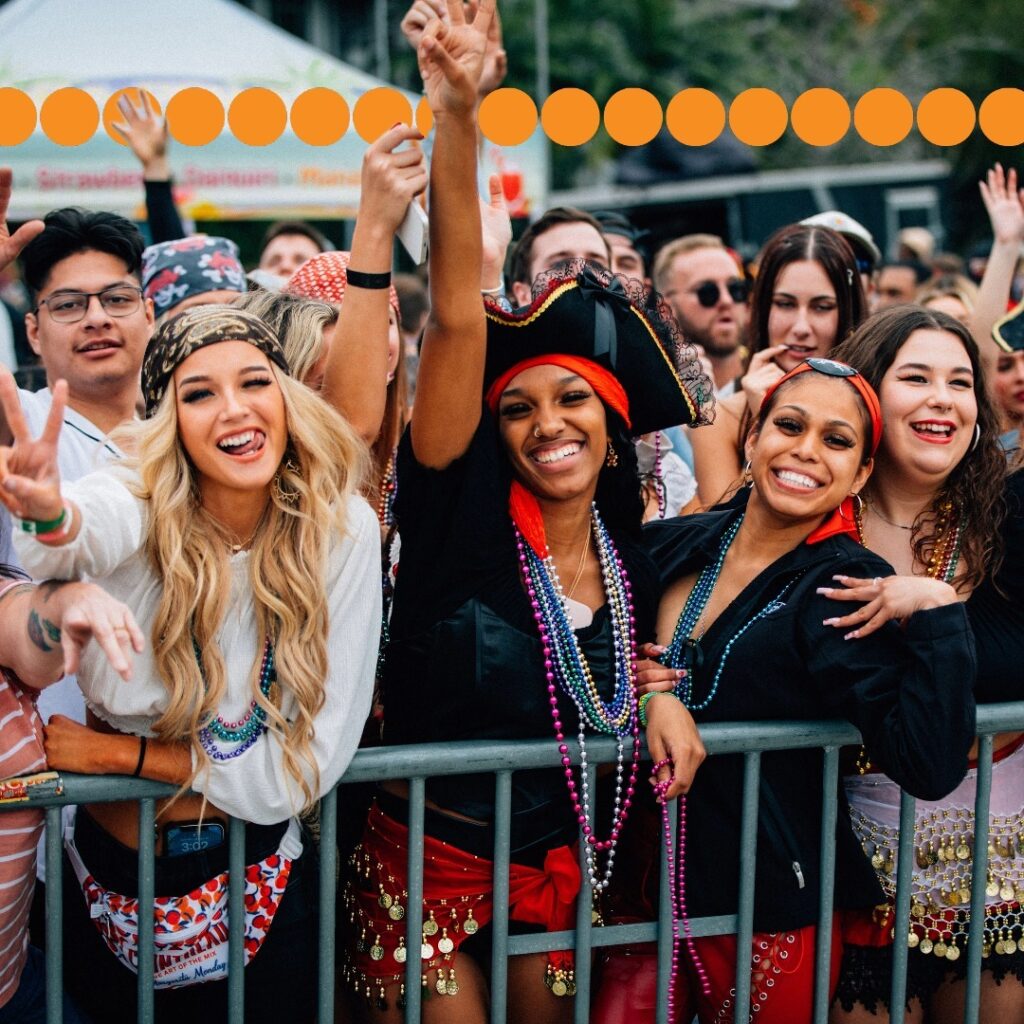 A joyful crowd of festival-goers at the Downtown Tampa Gasparilla Festival, adorned in pirate costumes and colorful beads, cheerfully celebrates the vibrant Parade of Pirates event.